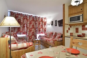 A cozy living room with a sofa, a small table, and a lamp. There is a kitchen area with a microwave and a sink.