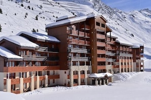A multi-story hotel with balconies, set against a snowy mountain backdrop.