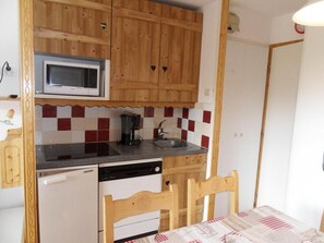 A compact kitchen with wooden cabinets, a microwave, a coffee maker, and a dishwasher.