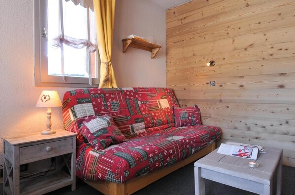 Una habitación acogedora con una pared de madera, un sofá rojo estampado, una mesita y una lámpara.