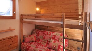Ein Stockbett mit rotem, gemustertem Bettbezug, Holzwänden und einem Fenster.