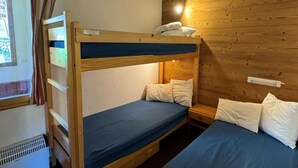 Une chambre avec un lit superposé, une tête de lit en bois, une petite table de chevet et une fenêtre avec des rideaux.