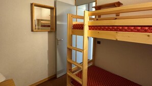 Una stanza con un letto a castello, una scala in legno, un tavolino e uno specchio appeso al muro.