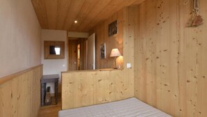 A wooden-paneled room with a bed, a desk, and a lamp. - 100m from ski slopes, 3rd floor, view ski slopes, balcony, tv, 51m², La Plagne (La Plagne)