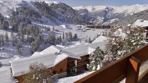 Paesaggio montano innevato con una baita di legno e una seggiovia sullo sfondo.