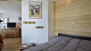A bedroom with a wooden headboard, a bed, a television on a wooden cabinet, and a framed painting on the wall.