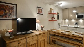 A modern kitchen with a flat-screen TV, wooden cabinets, and a dining area with a bench.