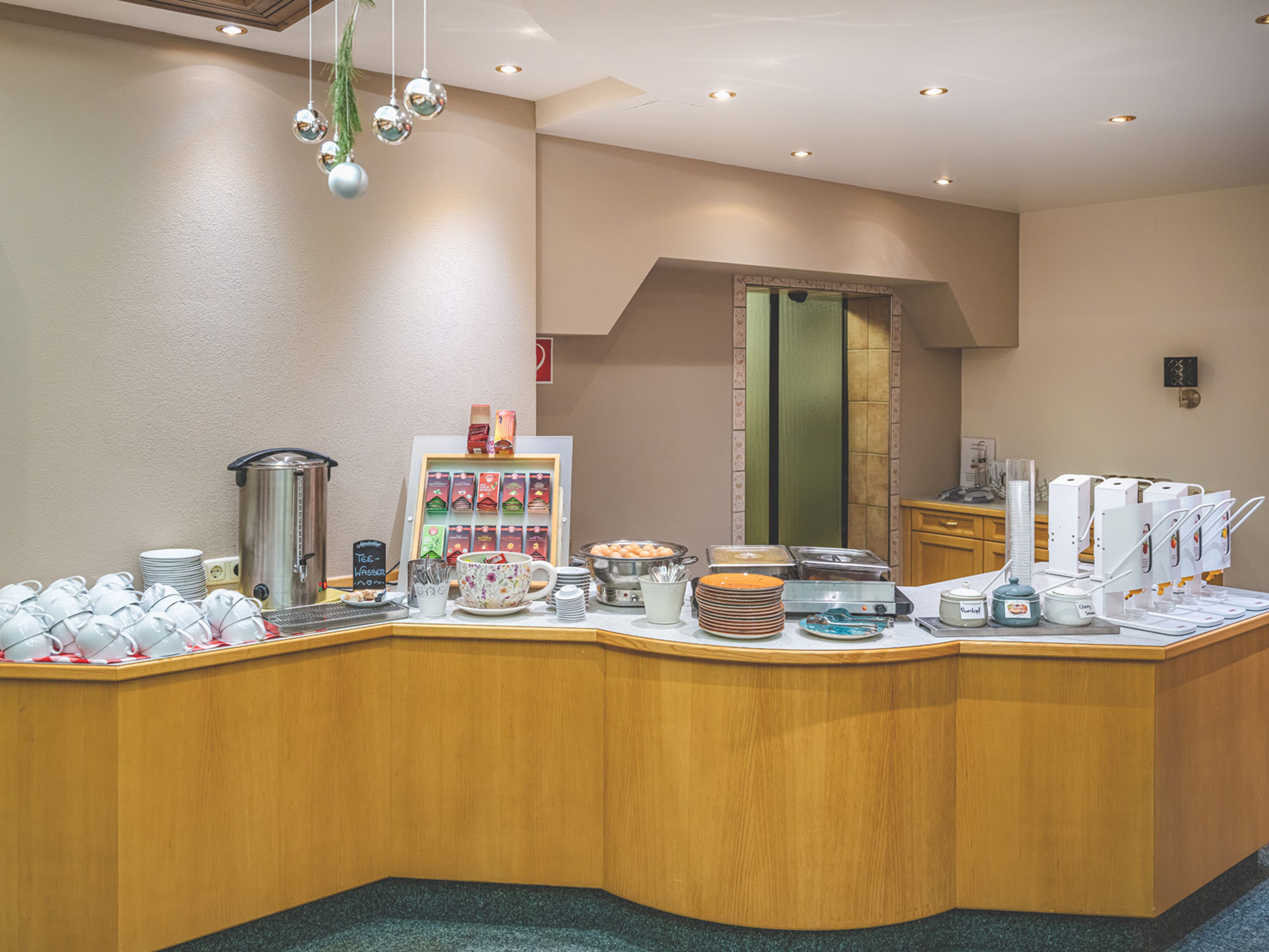A breakfast buffet area with various food and drink options, including coffee machines and a display of tea bags.