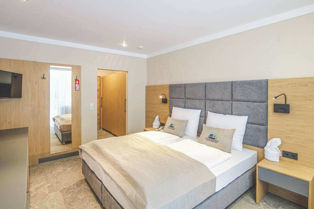 Hotellihuone, jossa on suuri sänky, puinen pääty, yöpöytä, televisio ja peili.