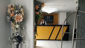 Vastaanottoalue, jossa on musta ja keltainen vastaanottotiski, vastaanottovirkailija ja vasemmalla puolella kukkakimppu.