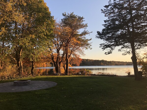 A lakeside park with trees, a circular stone fire pit, and a view of the lake. - Waterfront retreat on Wequaquet Lake. Kayaks included and close to Town/Beaches (Barnstable)