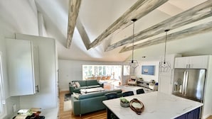 A modern kitchen with a marble island, wooden beams, and a dining area with a green sofa.
