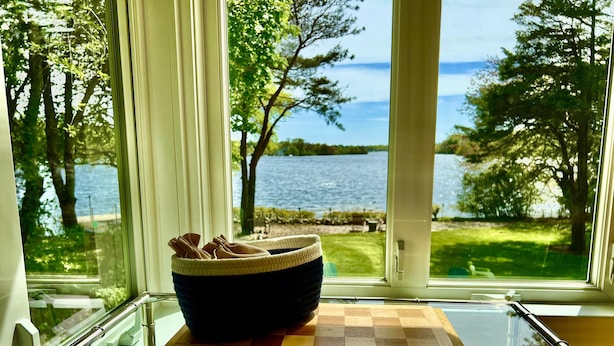 A chessboard on a windowsill with a view of a lake and trees.