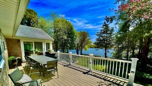 A deck with a table and chairs, a covered grill, and a view of a lake.