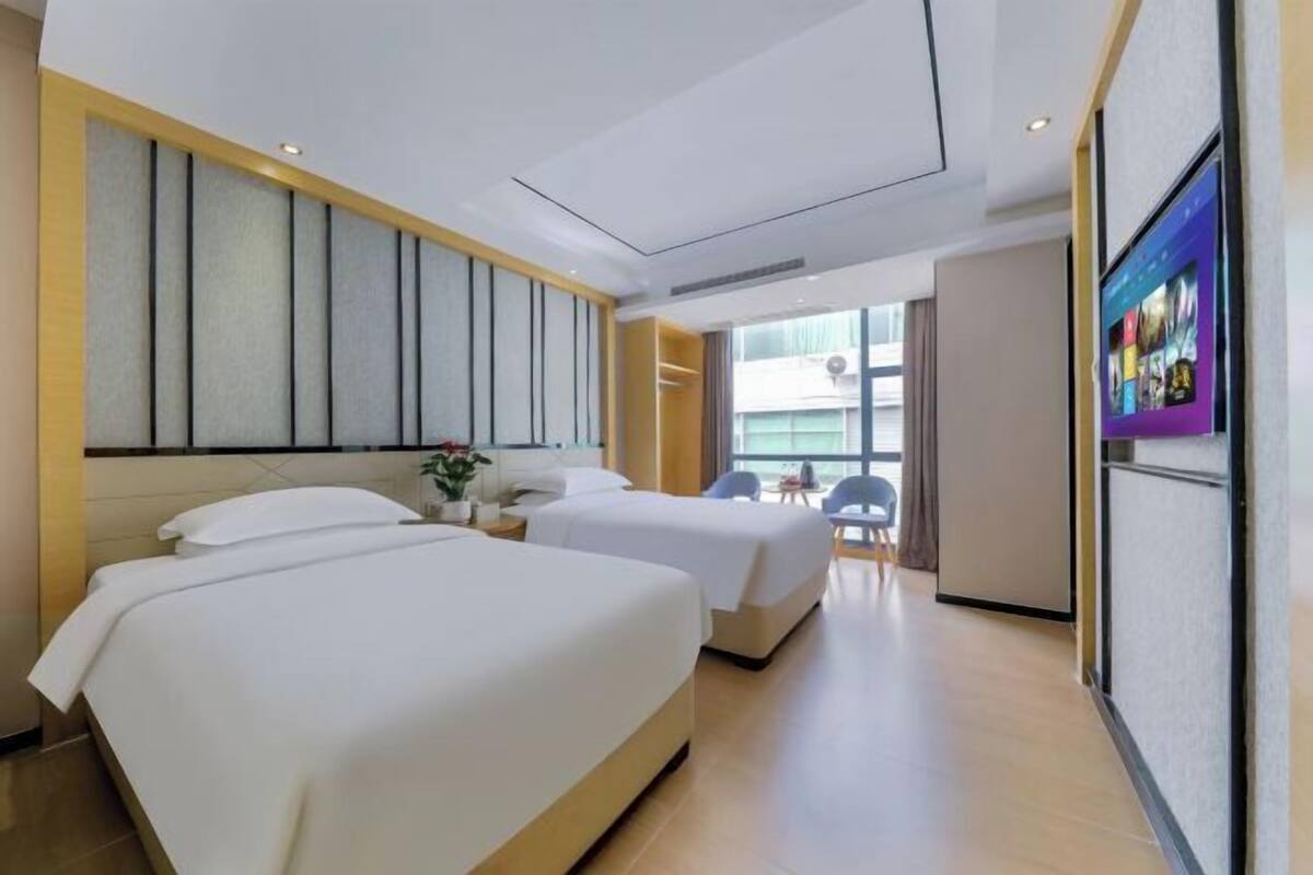 A hotel room with two beds, a TV, and a view of the outside.