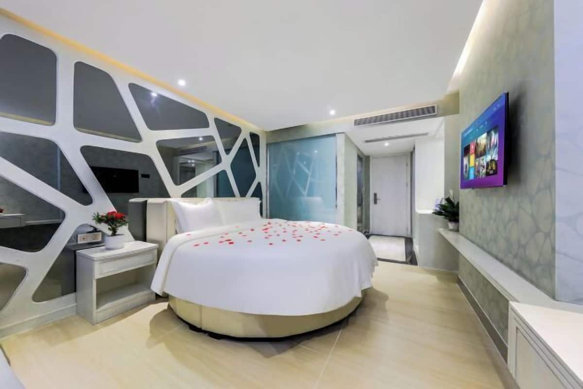 A modern bedroom with a round bed, a nightstand, a wall-mounted TV, and a unique geometric wall design.