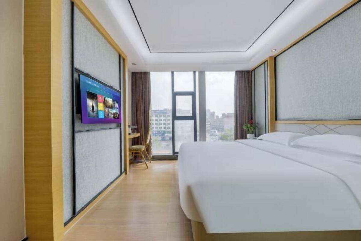 A hotel room with a large bed, a television on the wall, and a view of the city through the window.