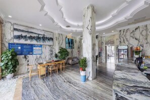 A hotel lobby with marble flooring, a reception desk, seating area, and a large pillar. - Royal Hotel (Shenzhen)