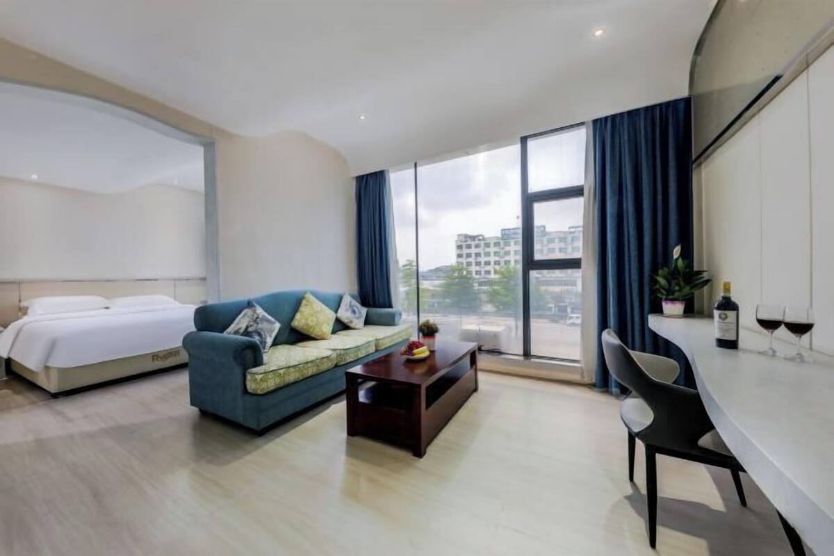 A hotel room with a bed, a sofa, a coffee table, a dining table, and a large window with curtains.