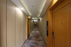 Un couloir d’hôtel avec un sol recouvert de moquette, des portes en bois et un panneau sur le mur.