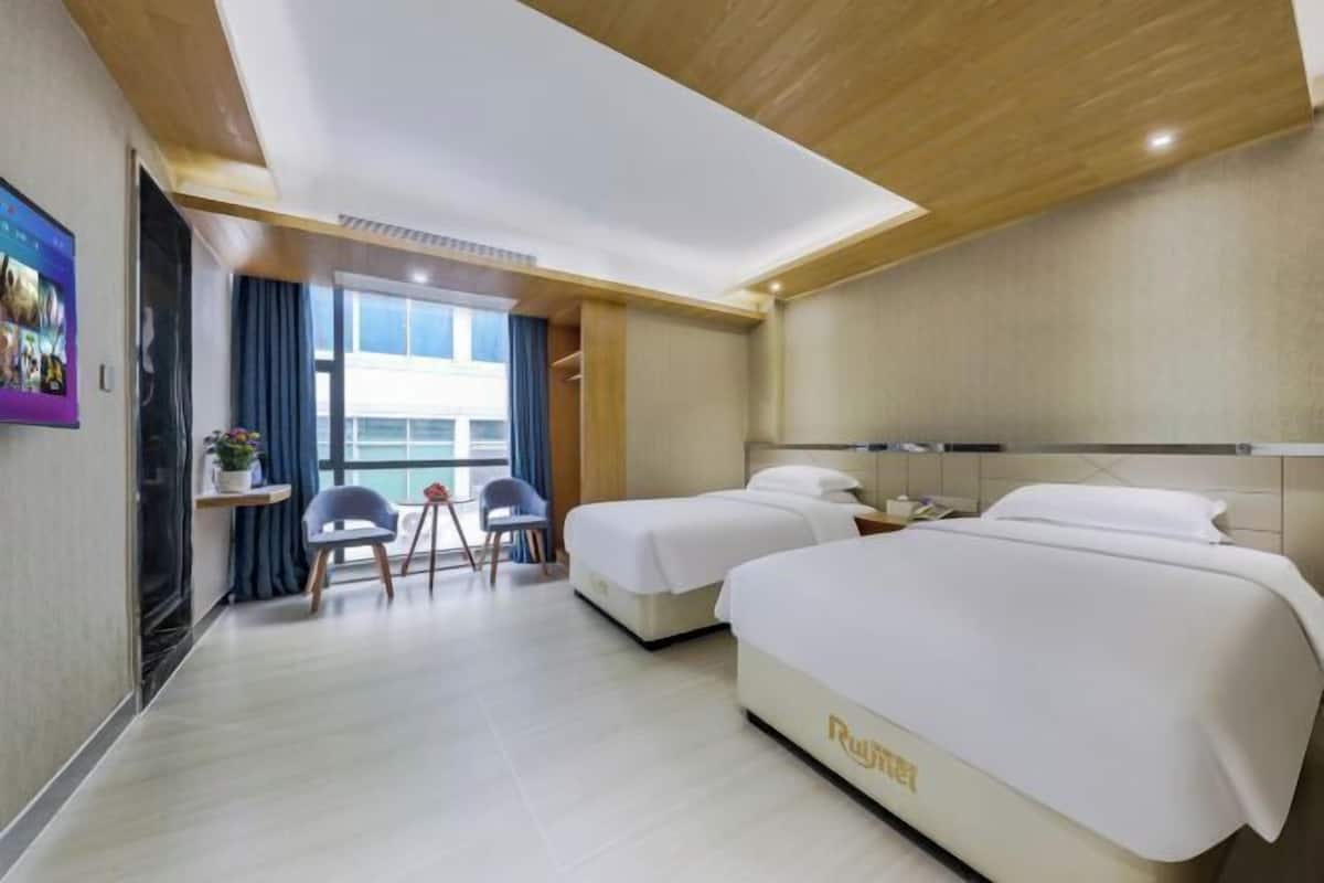 A hotel room with two beds, a desk, a chair, and a view of the city.
