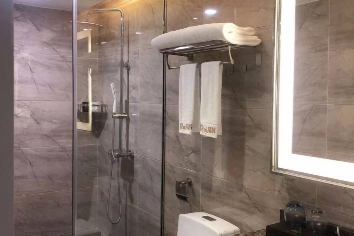 A modern bathroom with a glass-enclosed shower, marble walls, and a towel rack with towels.