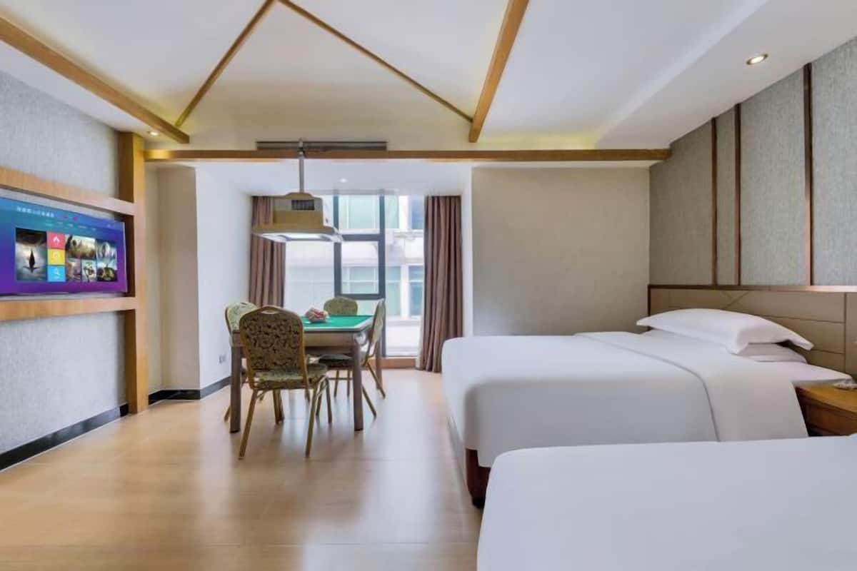 A hotel room with two beds, a desk with a chair, a television, and a large window.