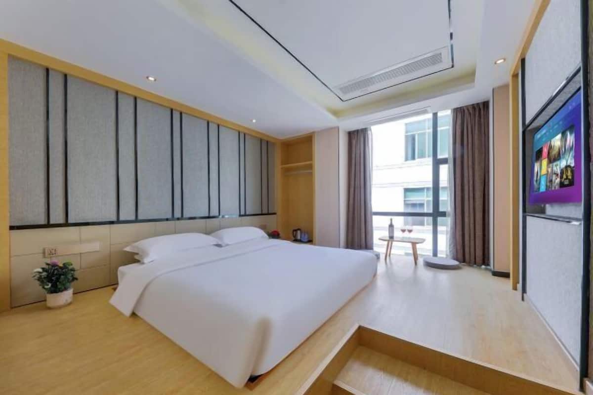 A modern hotel room with a large bed, a TV, a small table, and a window with curtains.