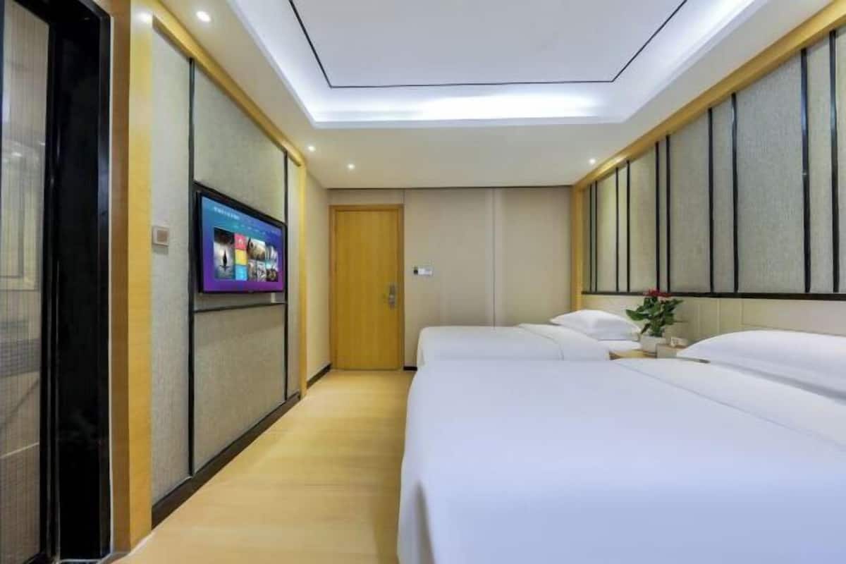 A hotel room with a bed, a TV on the wall, and a wooden floor.