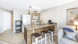 A compact kitchen with a wooden island, white appliances, and a bar stool seating area. - Gulf Views, Beach Chairs& Wagon, Steps to Pool& Beach, Spring Break Discount (Orange Beach)