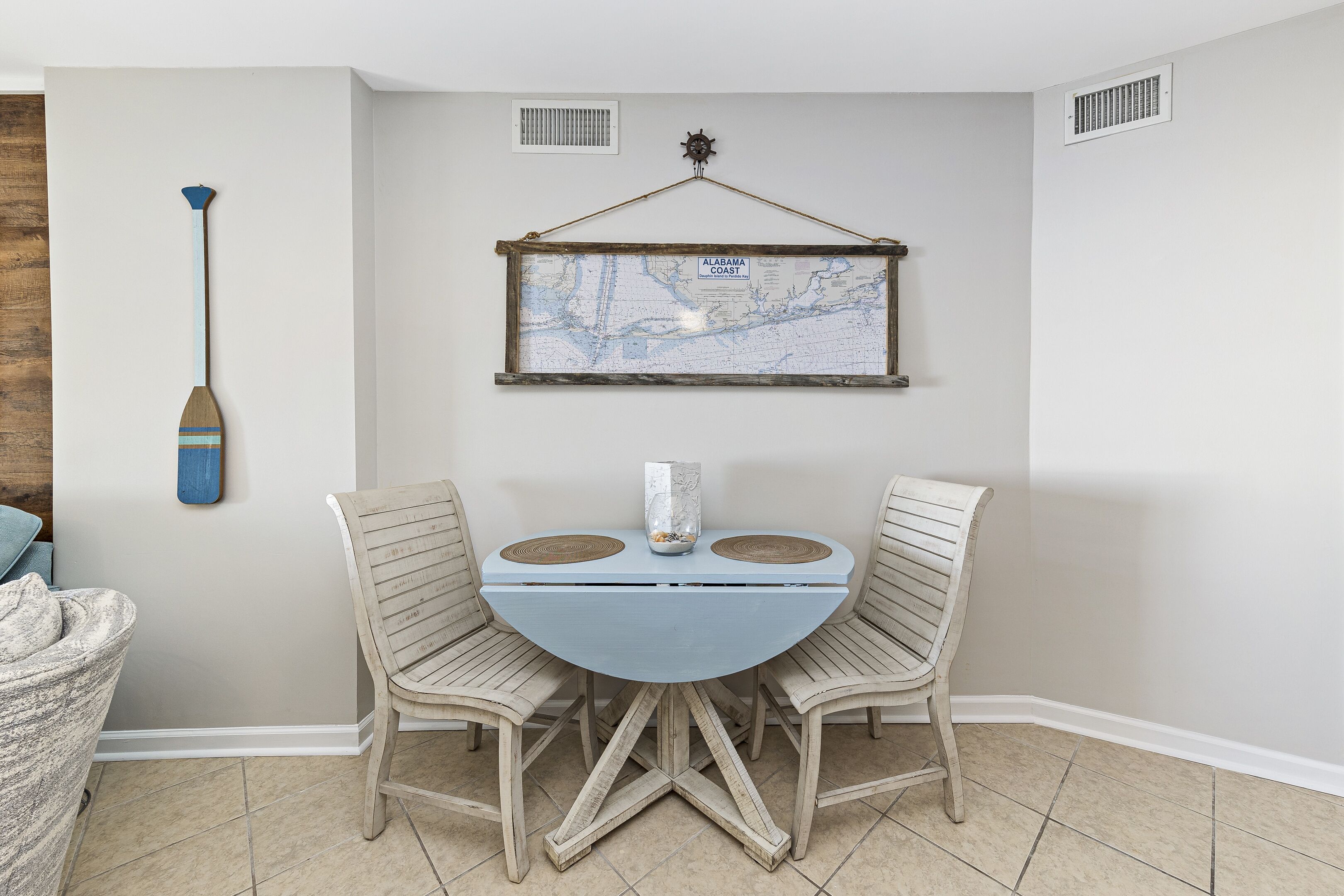 A dining area with a round table, four chairs, a map on the wall, and a paddle leaning against the wall.