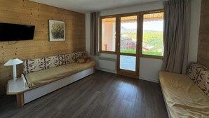A room with a wooden wall, a sofa, a bed, a TV, and a window with a view of greenery. - Ski-in/ski-out & foot of the slopes, 2nd floor, view ski slopes, balcony, tv, 35m², La Plagne (La Plagne)