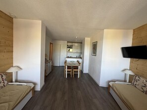 Ein kompakter Wohnbereich mit Küchenzeile, Essplatz und Wand-Fernseher.