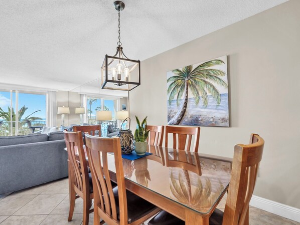 A dining area with a glass-top table, wooden chairs, and a hanging light fixture.
