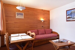 Um quarto aconchegante com parede de madeira, um sofá, uma mesa de jantar com cadeiras e uma mesinha com uma vela.