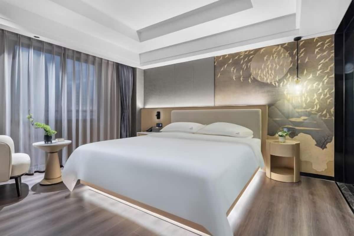 A modern hotel room with a large bed, a bedside table, a chair, and a decorative wall.