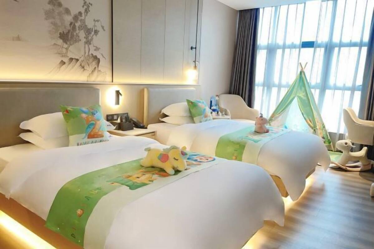A hotel room with two beds, a green canopy, a painting on the wall, and a window with curtains.