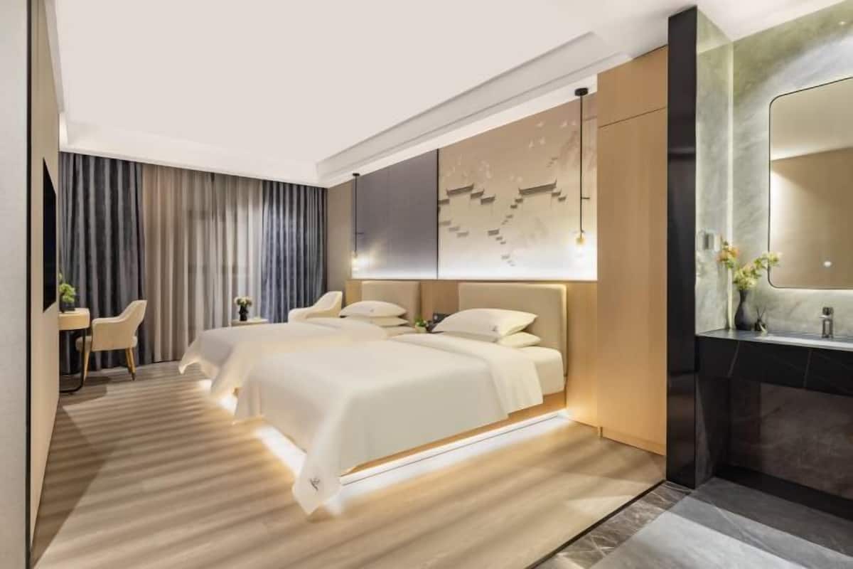 A modern hotel room with a large bed, a desk, and a vanity with a mirror.