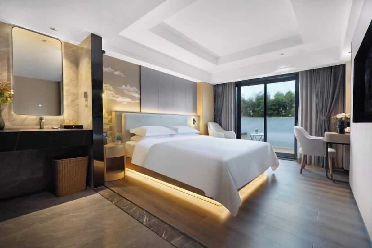 A modern hotel room with a large bed, a bathroom with a mirror, and a view of the outdoors.