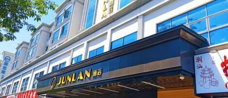 Un immeuble commercial avec une enseigne d’hôtel Junlan, des devantures de magasins et un ciel dégagé.