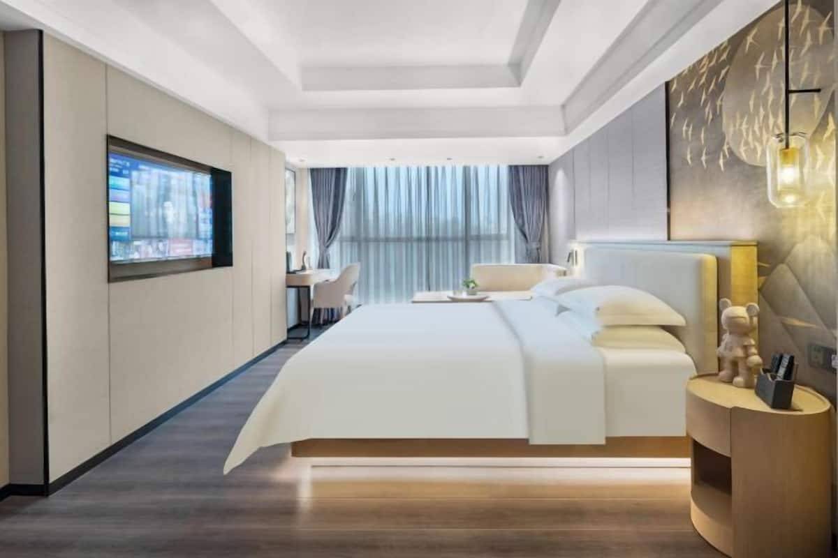 A modern hotel room with a large bed, a desk, and a TV mounted on the wall.