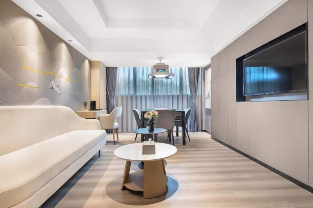 A modern hotel room with a sofa, a round table, a TV, and a large window.