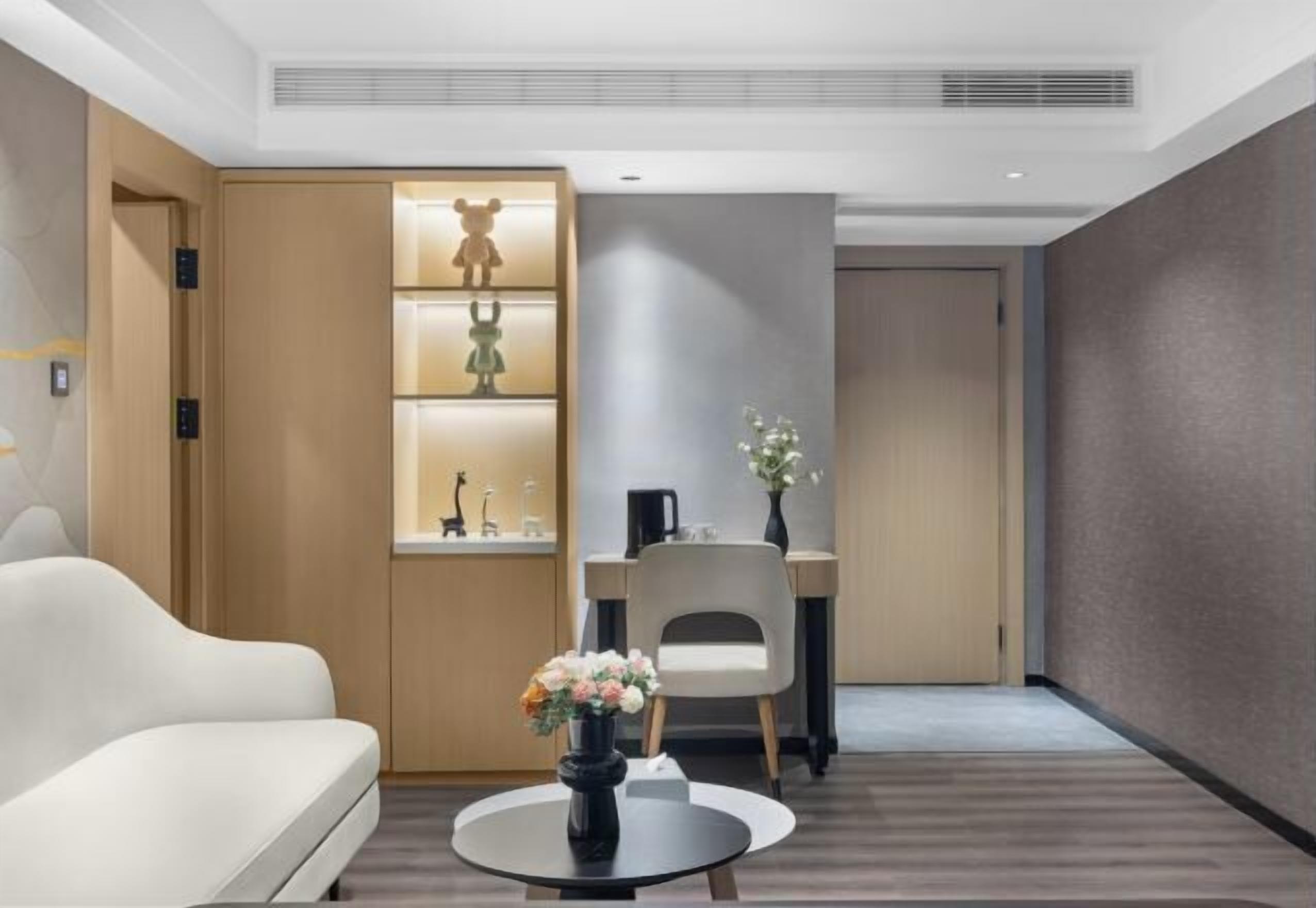 Un hotel moderno con sofá blanco, una mesa redonda con flores, un escritorio con silla y una pared con estantes que exhiben objetos decorativos.
