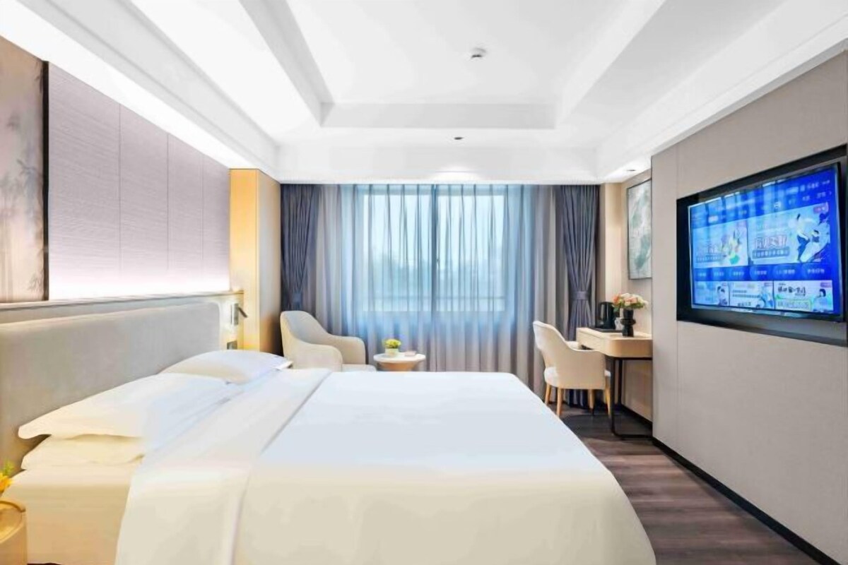 A hotel room with a bed, a desk, a chair, a TV, and a window with curtains.