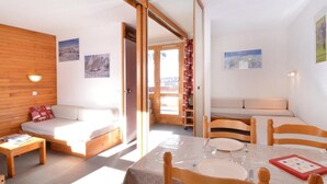 A cozy room with a wooden wall, a sofa, a dining table with chairs, and a view of the outside.