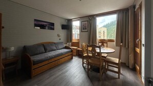 Una habitación acogedora con un sofá de madera, una mesa de comedor con sillas y una ventana con cortinas.
