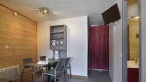 Una habitación con pared de madera, una mesa con sillas, una cafetera y un televisor montado en la pared.