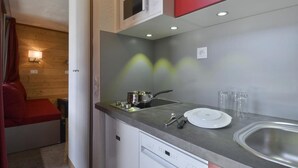 Una kitchenette compacta con microondas, estufa, pileta y muebles color rojo.