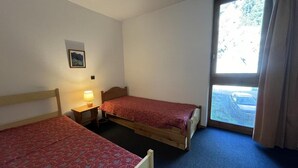 Een kamer met twee eenpersoonsbedden, een klein tafeltje met een lamp, een raam met gordijnen, en een foto aan de muur.