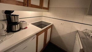 Een compacte keuken met witte tegels, een klein spoelgedeelte, een koffiezetapparaat en houten kastjes.